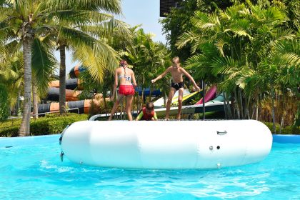 Kinder und Jugendliche springen auf einem weißen Wassertrampolin in einem Freibad und haben Spaß. Wassertrampolin bei Das Erlebnismanagement kaufen!