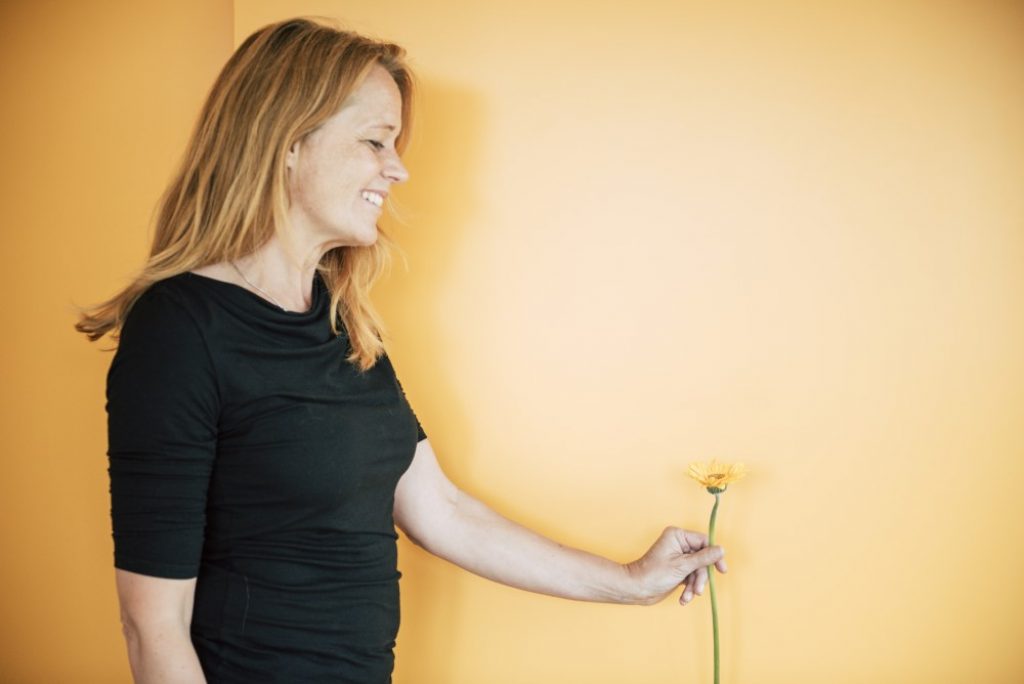 Mitarbeiterin Ulli mit Blume vor orangem Hintergrund