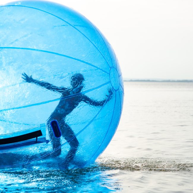 ein Junge in einem Aqua Zorbing Ball bewegt sich mit diesem Ball übers Wasser