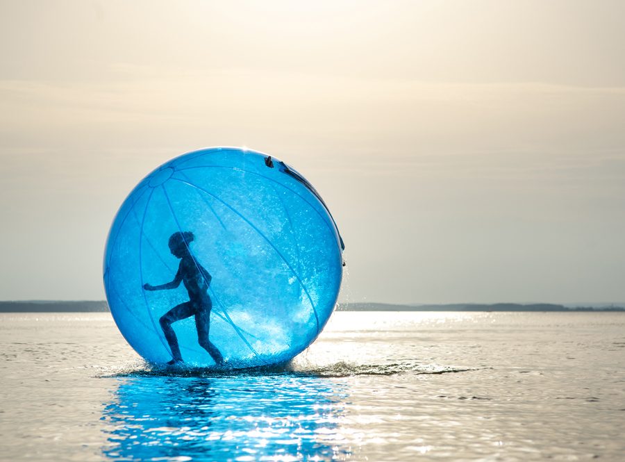 Mädchen in Aqua Zorbing Ball läuft mit dem Ball über einen See bei Sonnenuntergang