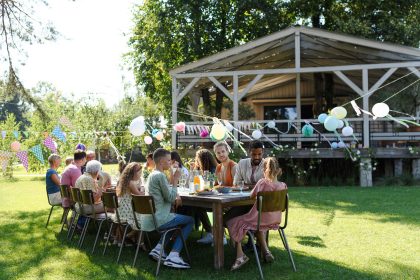 Family and friends sitting at the party table during a summer garden party outdoors decorations and beautiful wooden gazebo at background