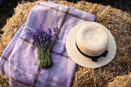 Bouquet of lavender flowers straw hat and blanket on hay bale